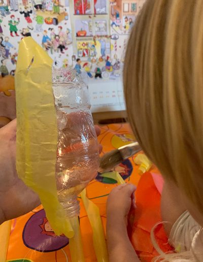 Ein Kind beklebt eine transparente Plastikflasche mit gelben Transparentpapier.